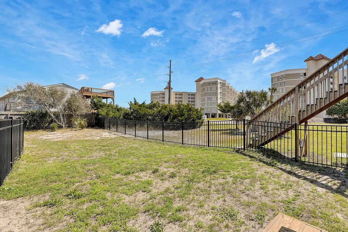 An expansive grassy area is surrounded by a secure, fenced perimeter, with a staircase leading up to the home. The open space is ideal for outdoor games, barbecues, or letting children and pets play freely in the sunshine.