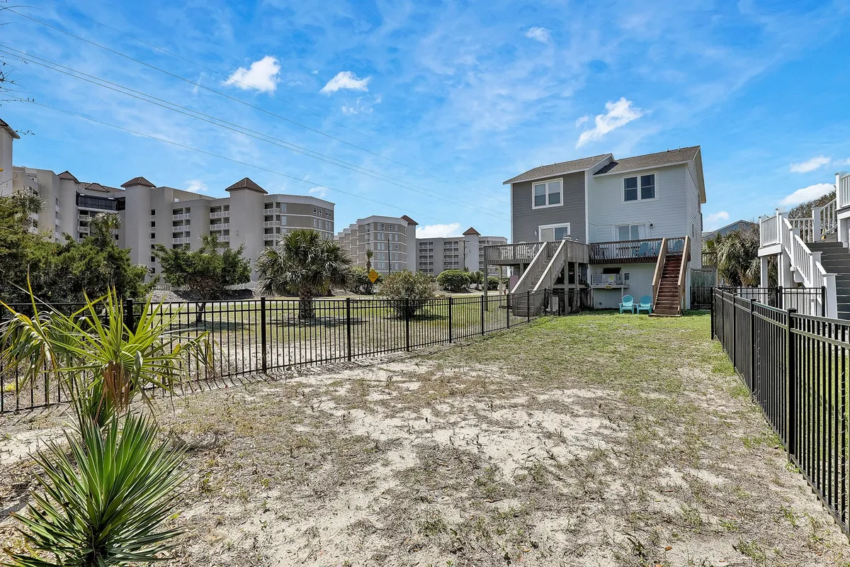 An exterior shot featuring a fenced private yard with palm trees, the house itself, and a staircase. The setting is ideal for outdoor family gatherings, with plenty of space for kids and pets to play safely while adults relax under the palms.