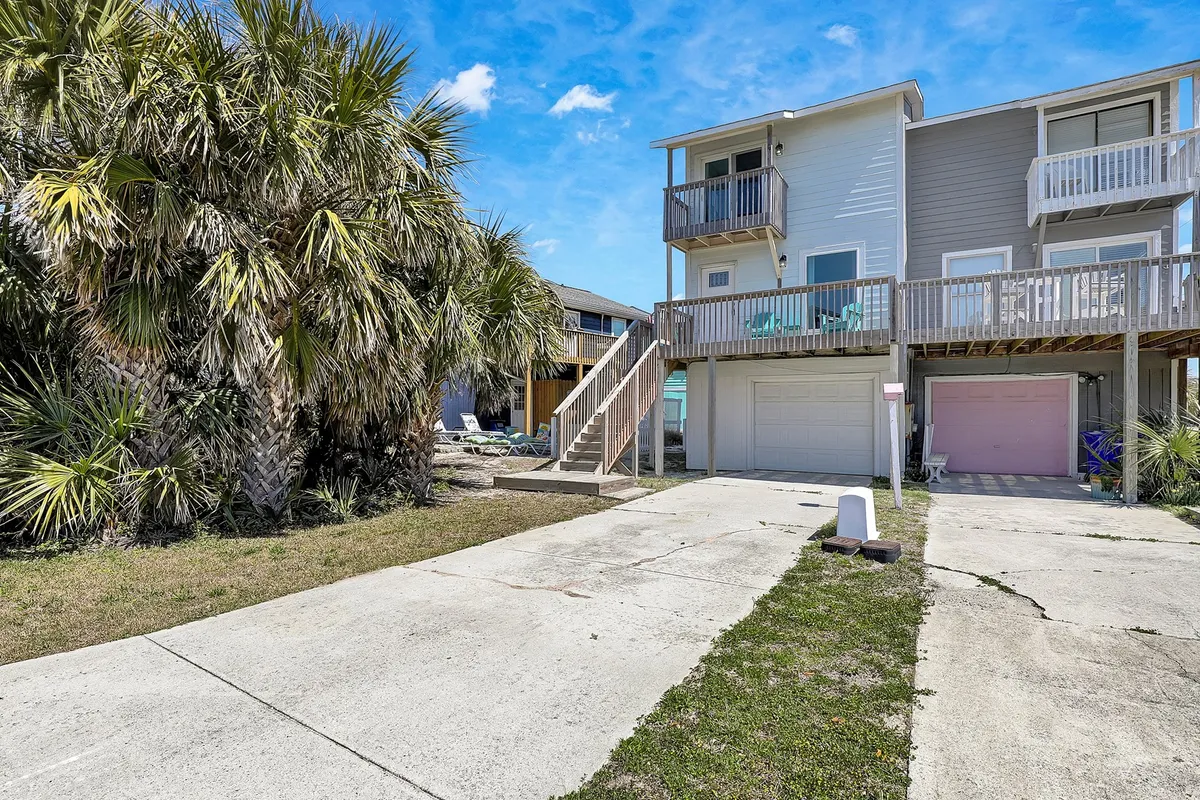 A relaxed view of palm trees, a balcony with seating, a staircase, and a garage, all set against a sunny backdrop. The scene suggests a welcoming home base for family gatherings, outdoor relaxation, and easy beach access.