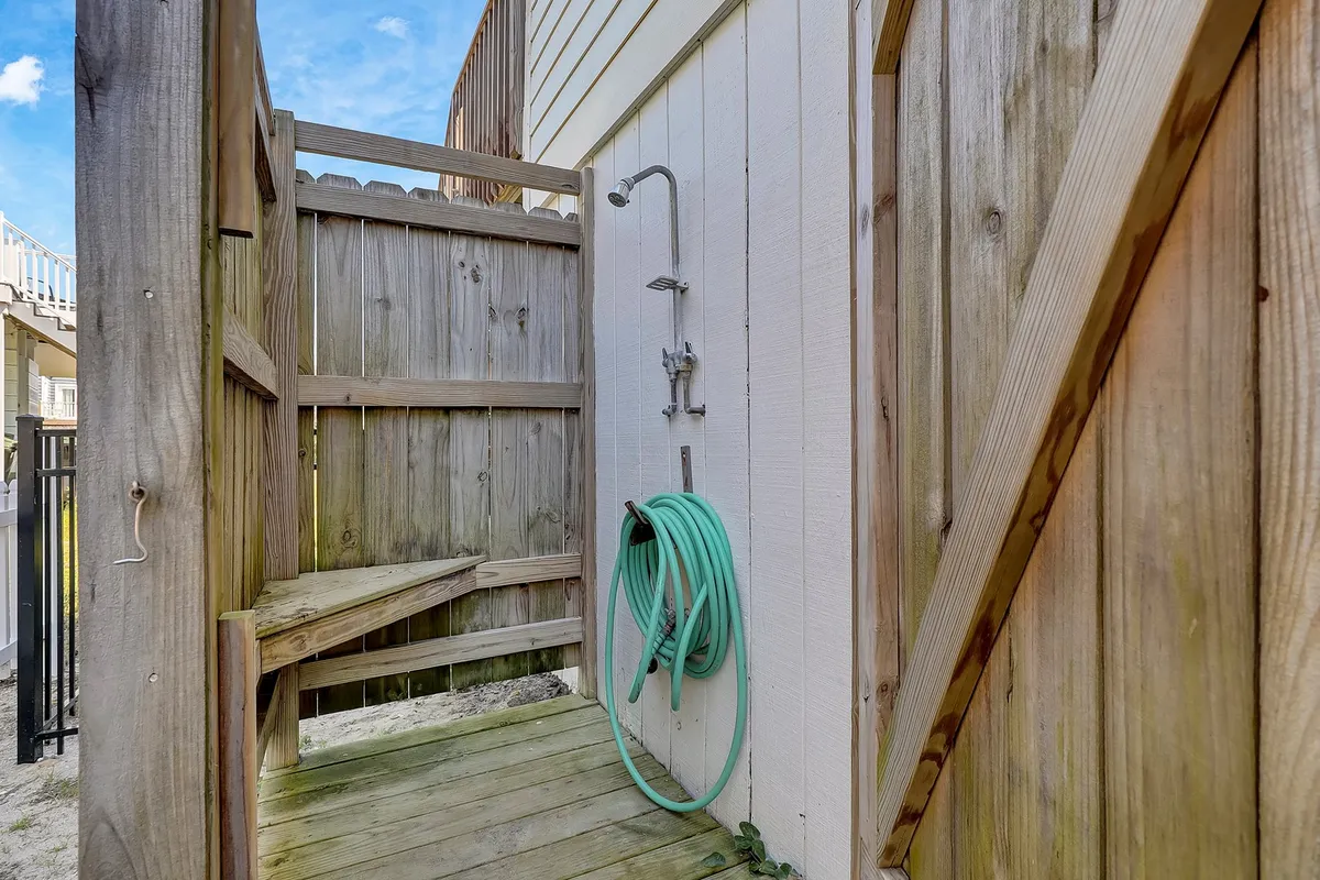 An inviting outdoor shower with a wooden bench and green garden hose set among sunny surroundings, perfect for rinsing off sand after a beach day. The casual, relaxed vibe hints at a comfortable, value-oriented beach lifestyle.