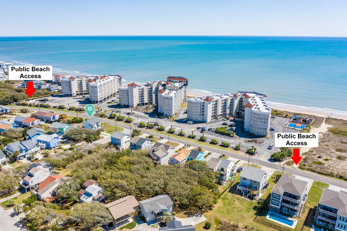 This image captures a vibrant exterior scene with a public beach access point, the ocean in the background, and nearby residential buildings. Family groups are visible preparing for beach activities and water sports, emphasizing easy access and the lively atmosphere.