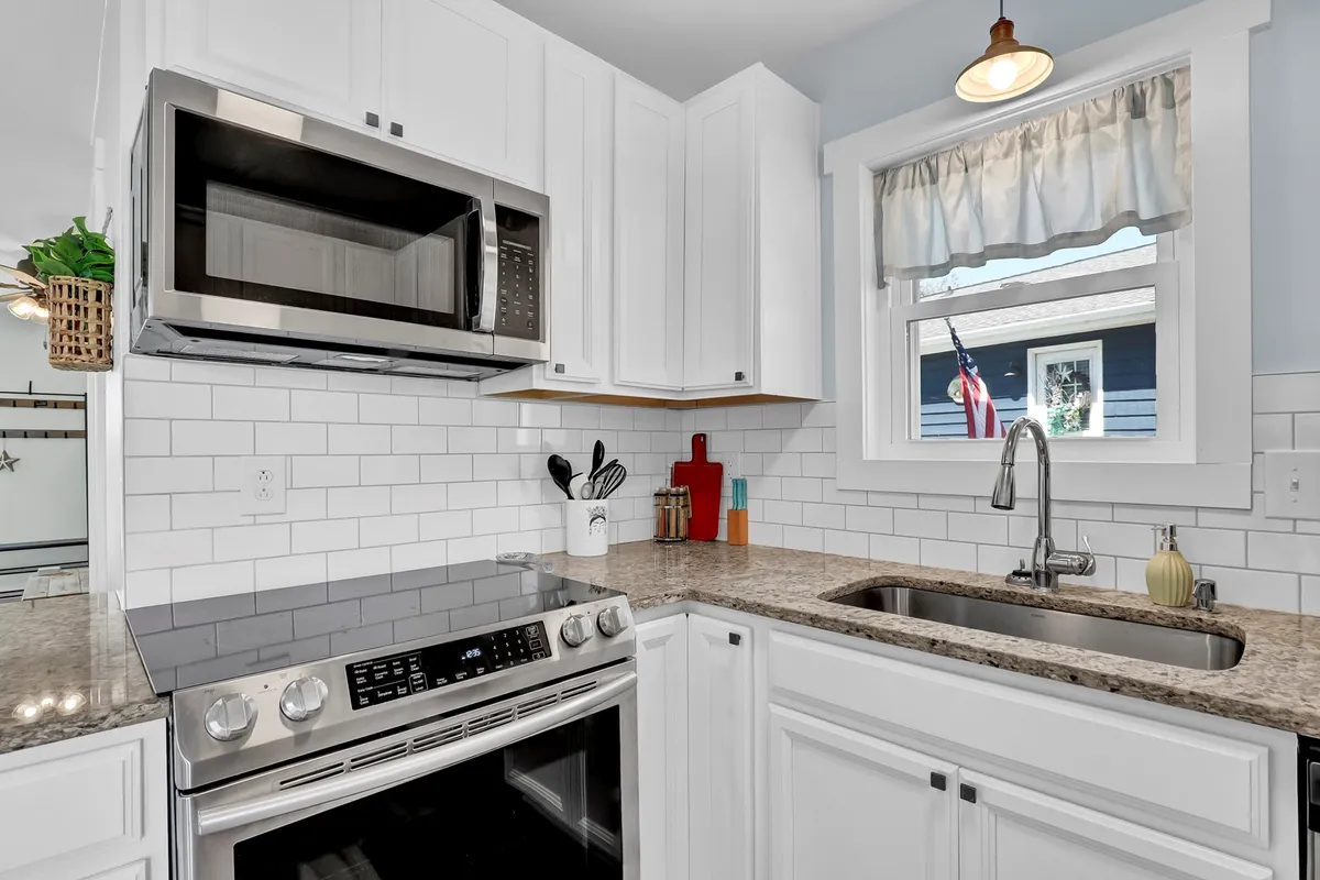 A warm, welcoming kitchen with stainless steel appliances, granite countertops, white cabinetry, and decorative items on the countertop. The space is designed for enjoyable meal prep and socializing, with everything needed for cooking or unpacking takeout close at hand.