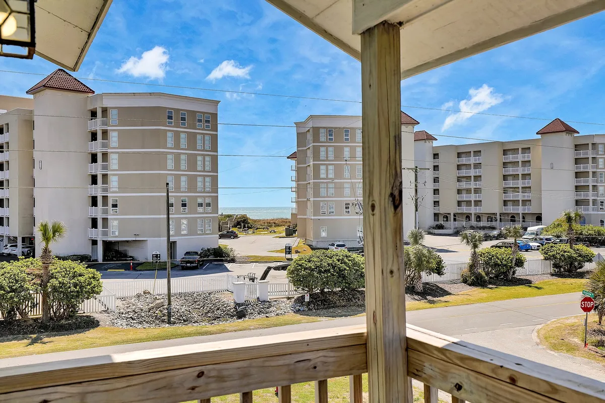 This exterior view showcases an expansive ocean vista framed by palm trees and surrounding coastal buildings. The image captures a tranquil moment, likely from a balcony or deck, overlooking the sparkling water and lively beachfront below.