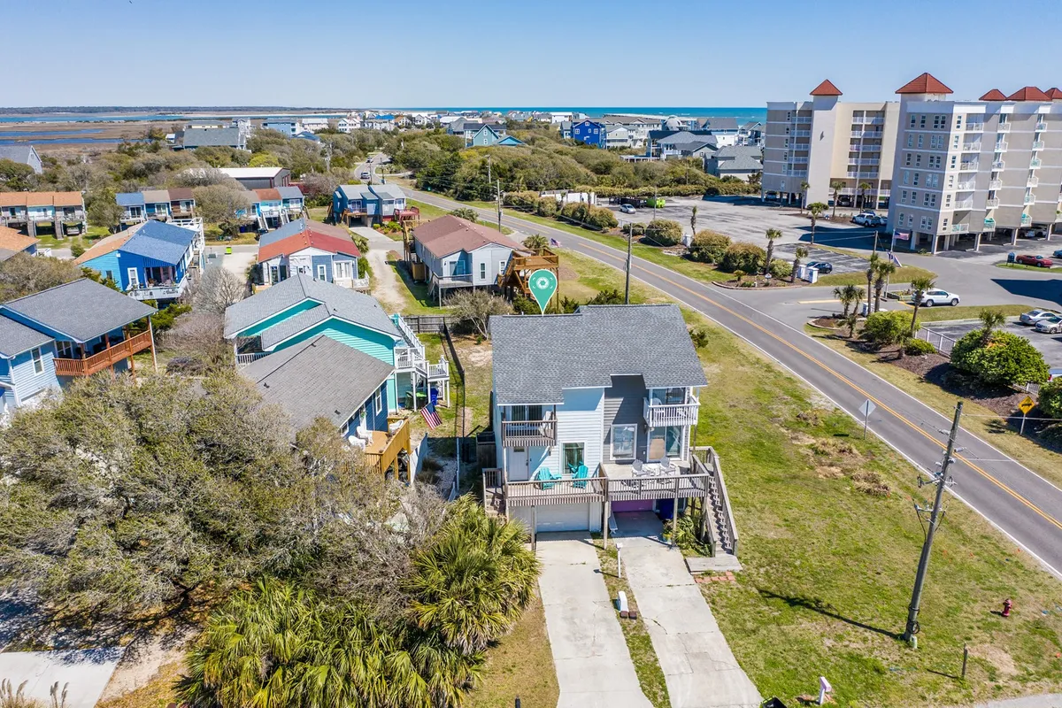 A bright, cheerful exterior scene featuring colorful beach houses, lush palm trees, a road leading directly to the ocean, and the sea in the background. The mood is vibrant and welcoming—perfect for showcasing the local neighborhood and easy access to pet-friendly outings, parks, and restaurants nearby.