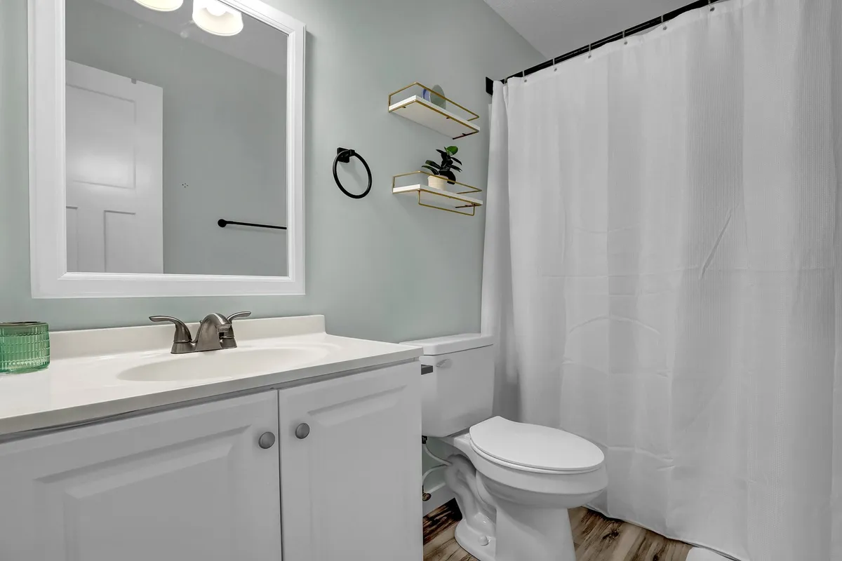 A sparkling clean bathroom with a vanity and sink, mirror, shower curtain, and floating shelves. The space is calming and well-lit, inviting moments of self-care and refreshment.